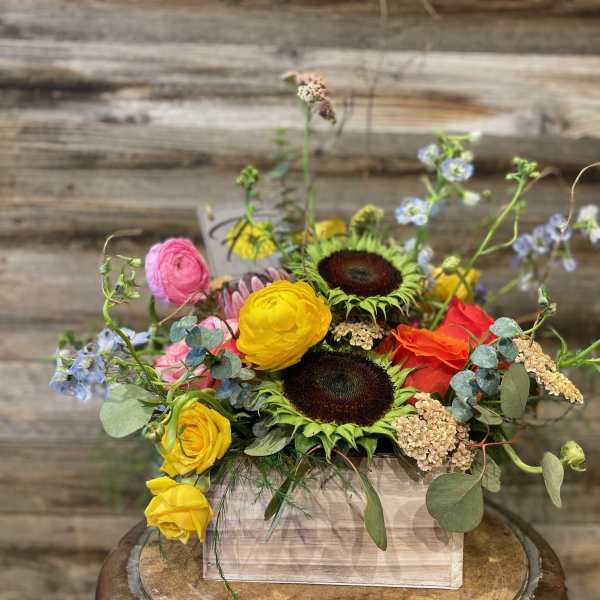 Mixed bouquet in a wooden box with sunflowers, roses, and blue flowers