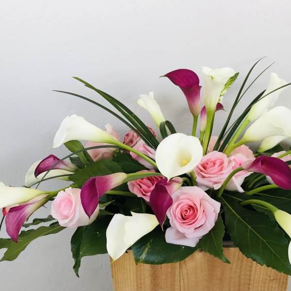 Pink roses and white-purple calla lilies in a wooden container