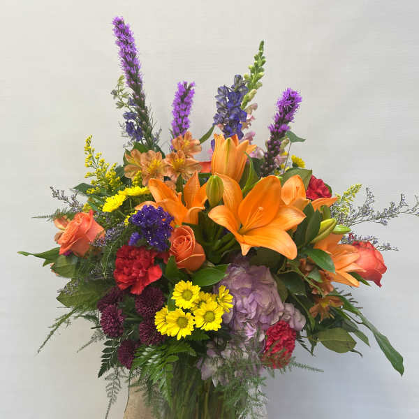 Colorful mixed bouquet in a glass vase with orange lilies and purple flowers
