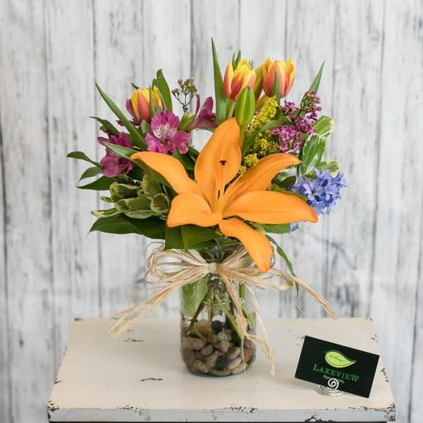 Mixed bouquet with orange lily and colorful tulips in a glass vase