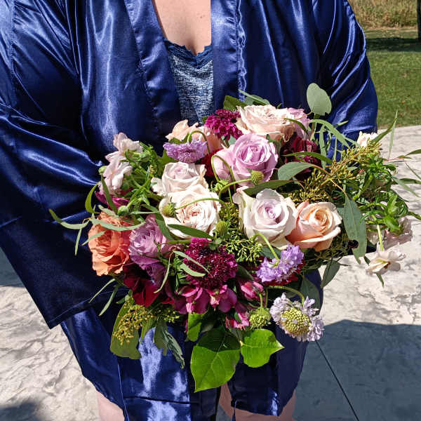 Person holding a bouquet of pink and peach roses with purple flowers