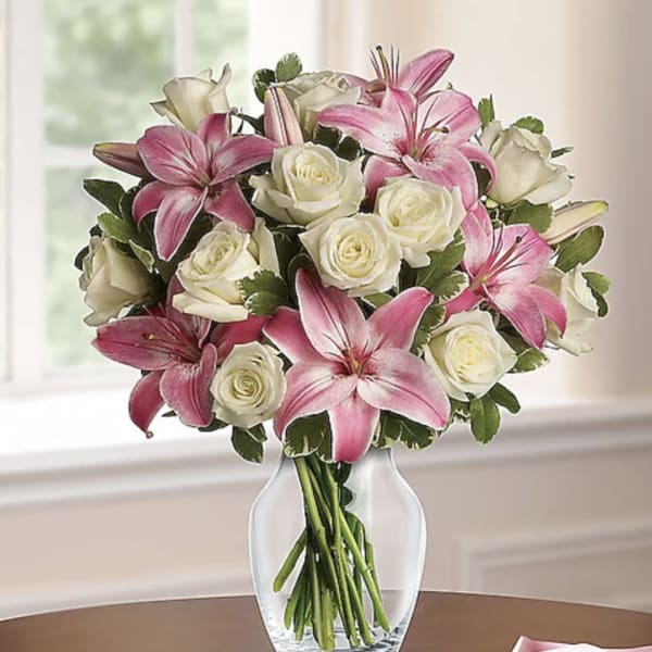 Pink lilies and white roses arranged in a clear glass vase on a table.