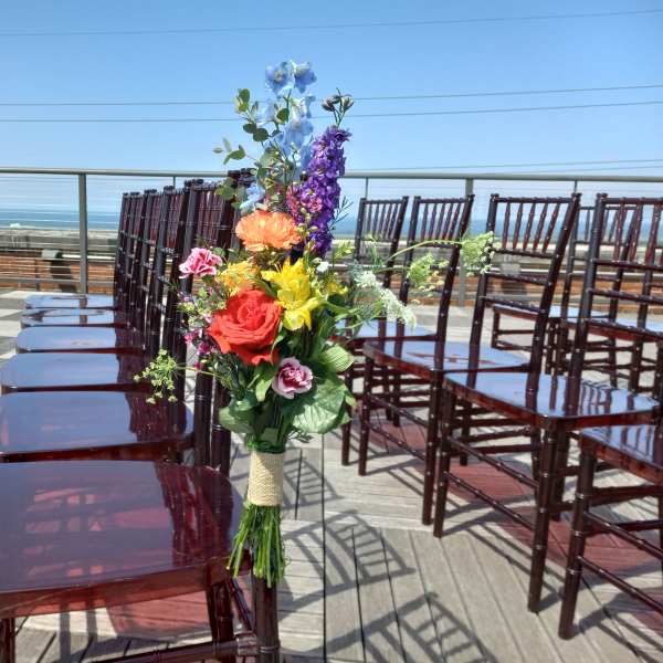 Colorful floral arrangement tied to a chair at an outdoor ceremony.