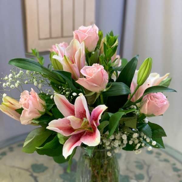 Pink roses and pink-and-white lilies arranged in a clear glass vase