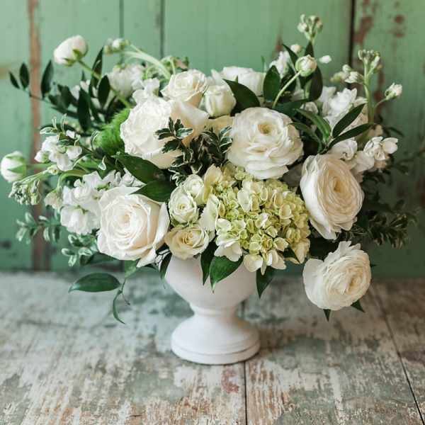 White roses and ranunculus arranged in a white pedestal vase