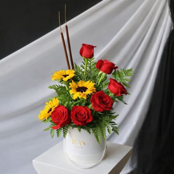 Red roses and yellow sunflowers arranged in a white hatbox with tall incense sticks