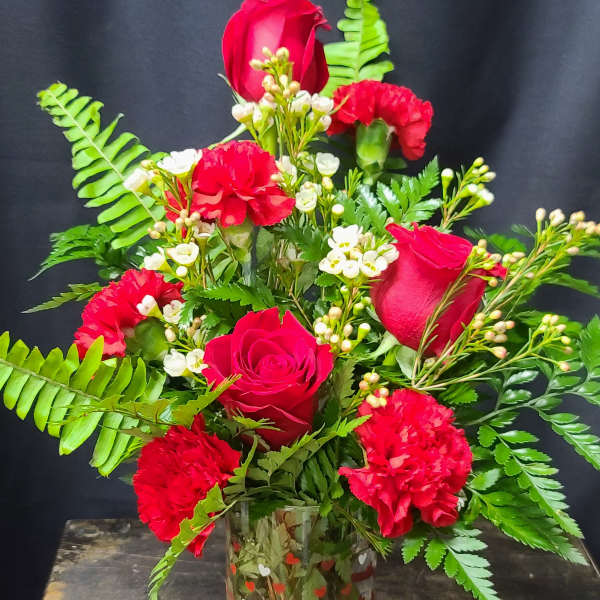 Red roses and carnations in a clear glass vase with fern foliage
