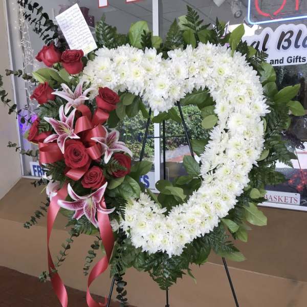 Heart-shaped floral wreath with white chrysanthemums, red roses, and pink lilies on an easel