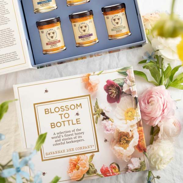 Gift box with six honey jars beside floral packaging