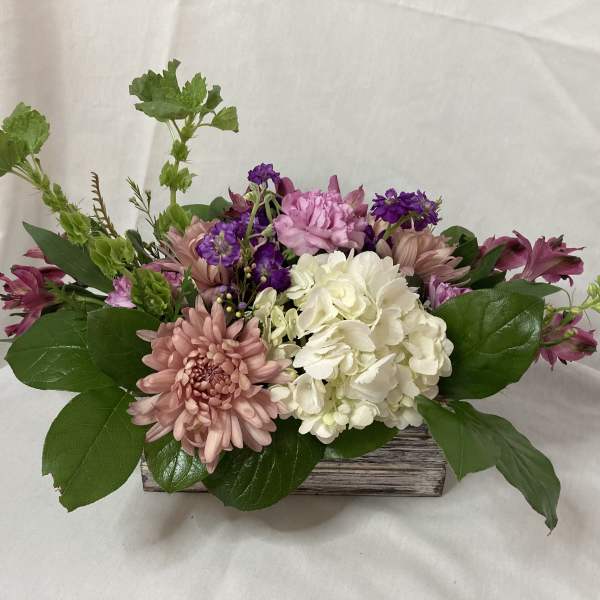 Mixed pink, white, and purple flowers arranged in a low wooden container