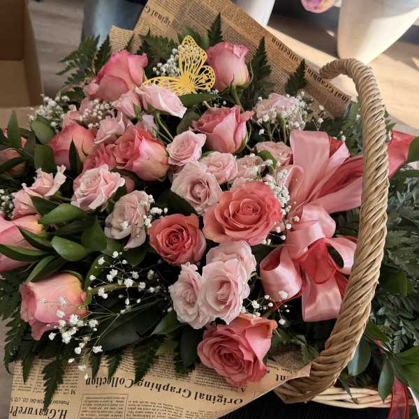 Low basket of pink roses and spray roses with baby's breath, pink bow, and yellow butterfly accent