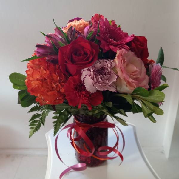Bouquet of red, pink, and orange flowers in a glass vase with ribbon