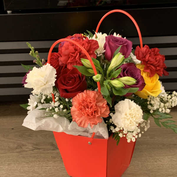 Colorful flower arrangement in a red handled gift bag
