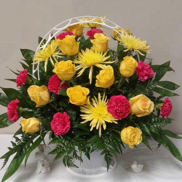 Yellow roses, pink carnations, and yellow spider mums in a white basket arrangement
