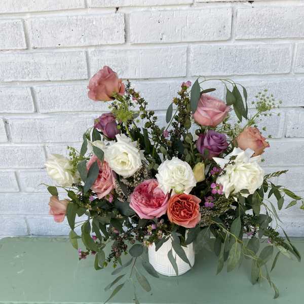 Mixed rose arrangement in a white vase with trailing greenery