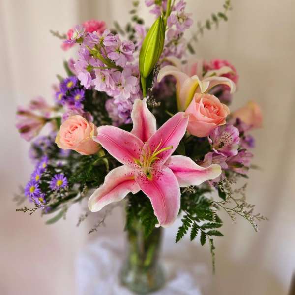 Pink lily bouquet with roses and purple filler flowers in a glass vase
