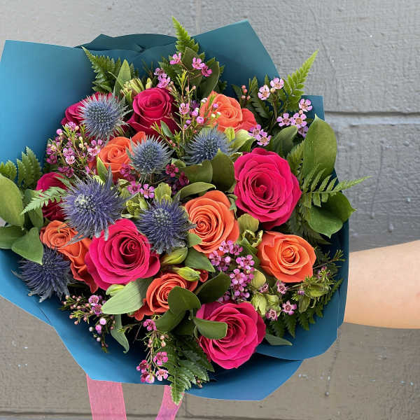 Bouquet of pink and orange roses with blue thistle in teal wrap