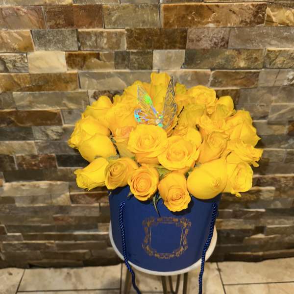 Yellow roses arranged in a blue hatbox with a butterfly pick