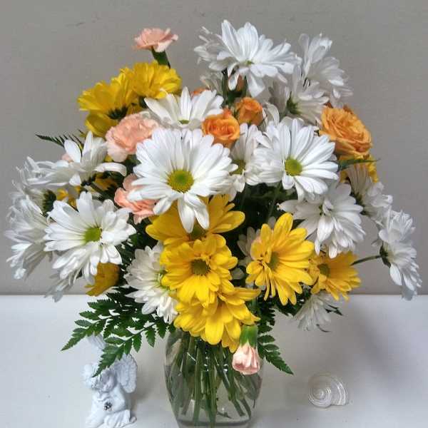 Bouquet of white and yellow daisies with peach accents in a glass vase