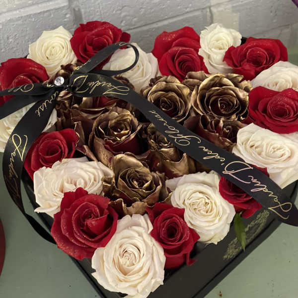 Heart-shaped box filled with red, white, and gold roses tied with a black ribbon