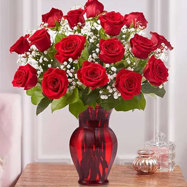 Red roses arranged in a red glass vase with baby's breath
