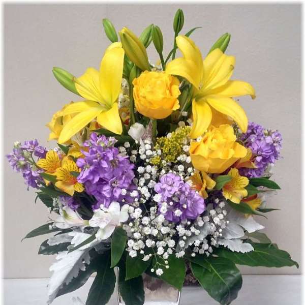 Yellow lilies and purple flowers in a silver vase