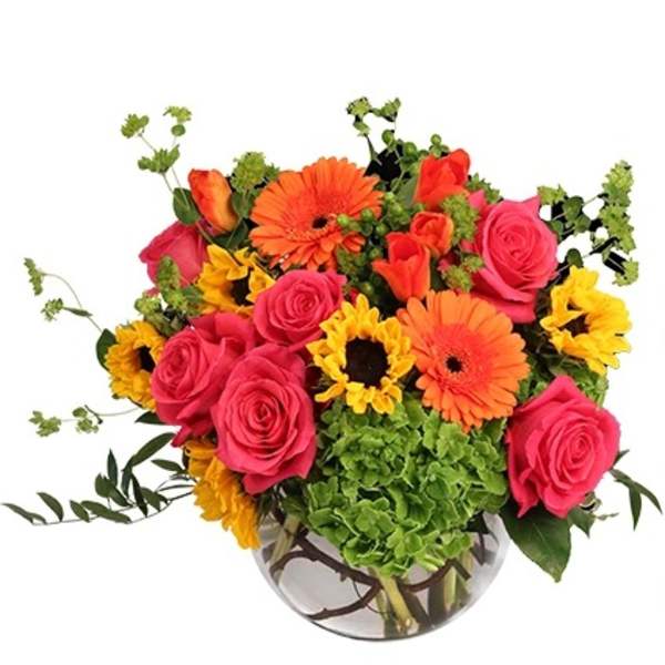 Bright mixed bouquet in a round glass vase with roses, gerbera daisies, and sunflowers
