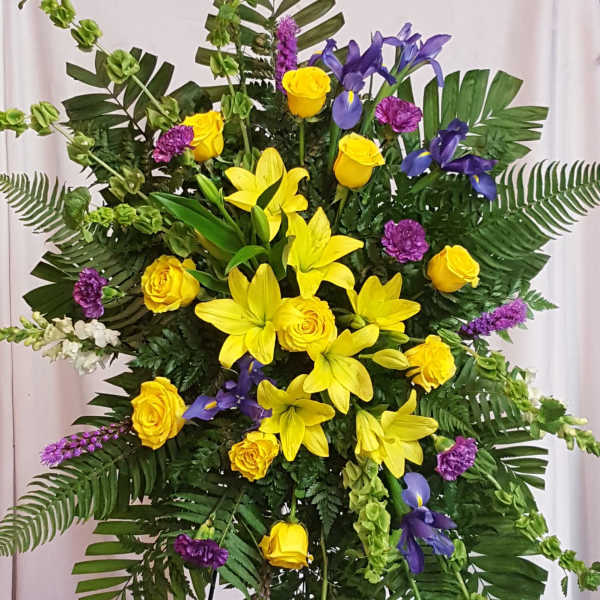 Large standing floral spray with yellow roses, lilies, and purple flowers