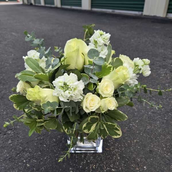 White and pale yellow floral arrangement in a clear square vase