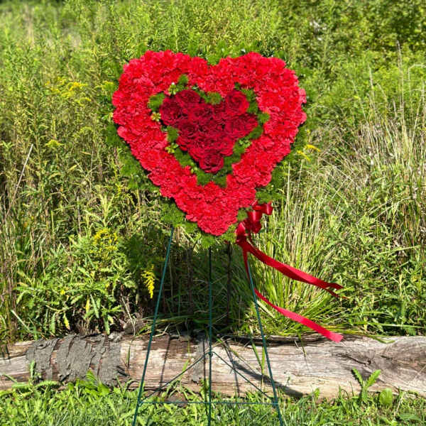 Standing heart-shaped red floral wreath with roses and carnations on a wire easel.