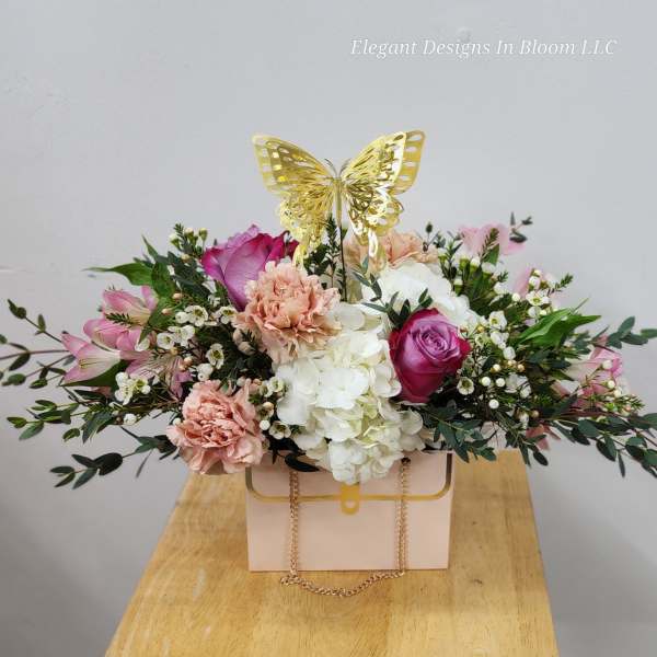 Pink and white floral arrangement in a box with a gold butterfly topper