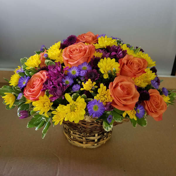 Basket arrangement of orange roses, yellow daisies, and purple flowers