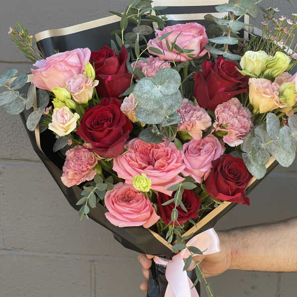 Handheld bouquet of pink and red roses with eucalyptus and a pink ribbon