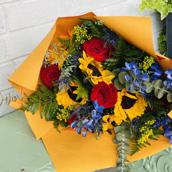 Bouquet of red roses, sunflowers, and blue flowers wrapped in orange paper