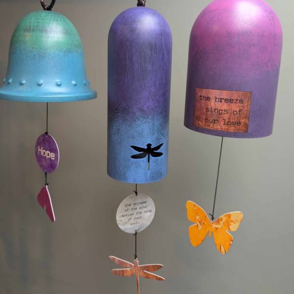 Three colorful hanging wind chimes with bell-shaped tops and dangling charms