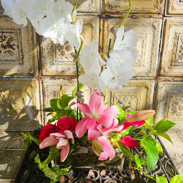 Pink lilies, red roses, and white orchids in a low arrangement