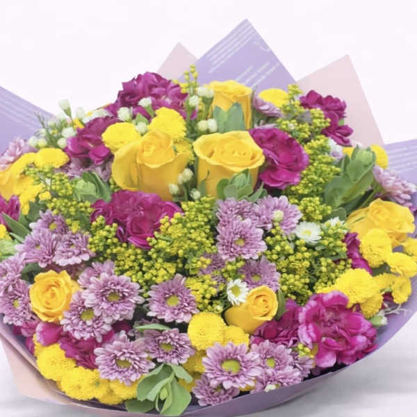 Bouquet of yellow roses, purple chrysanthemums, and pink flowers wrapped in pastel paper