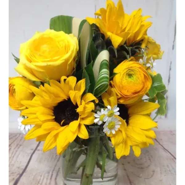 Yellow sunflowers, rose, and ranunculus arranged in a clear glass jar vase