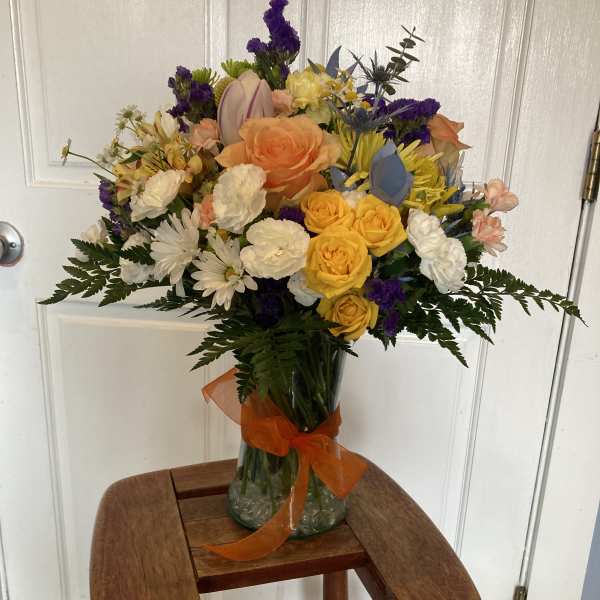 Mixed bouquet of roses, daisies, and purple filler flowers in a glass vase