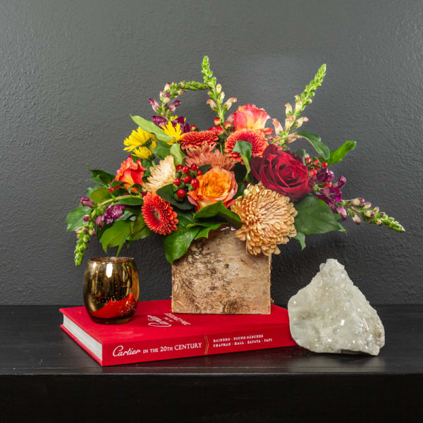 Mixed bouquet in a rustic wooden vase with a gold candle holder and crystal decor