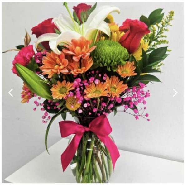 Mixed bouquet of lilies, roses, and daisies in a glass vase with a pink ribbon