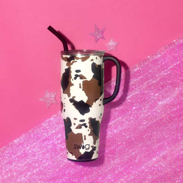 Cow-print travel tumbler with a black straw on a pink background