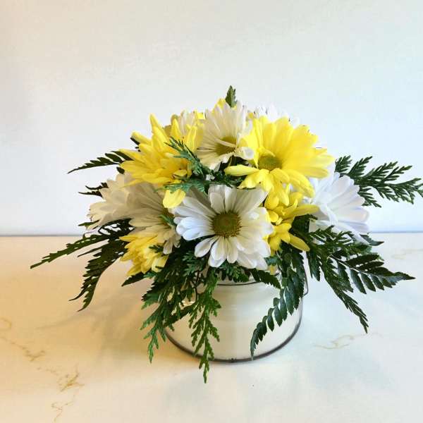Yellow and white daisies arranged in a low white container