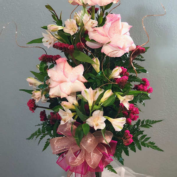 Tall pink and white rose and alstroemeria arrangement in a dark glass vase with glittery ribbons