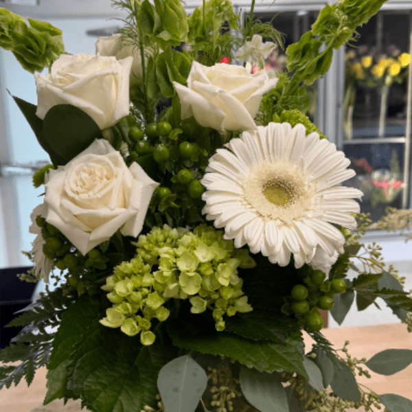 White roses, a white gerbera daisy, and green hydrangea arranged in a clear glass vase.