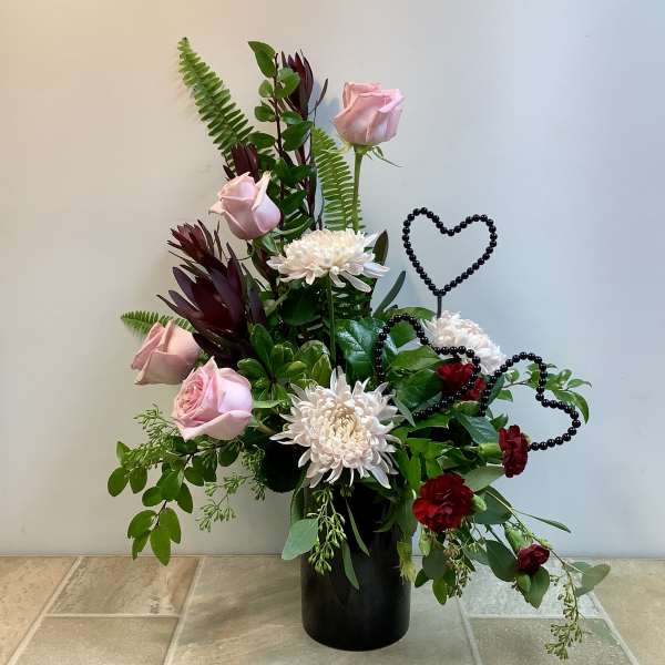 Pink roses and white chrysanthemums in a black vase with heart picks.