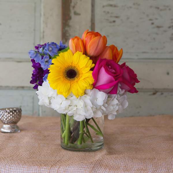 Mixed bouquet in a clear glass vase with yellow, pink, orange, blue, and white blooms