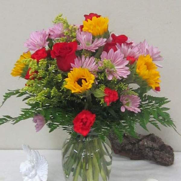Mixed bouquet of red roses, pink daisies, and yellow flowers in a glass vase