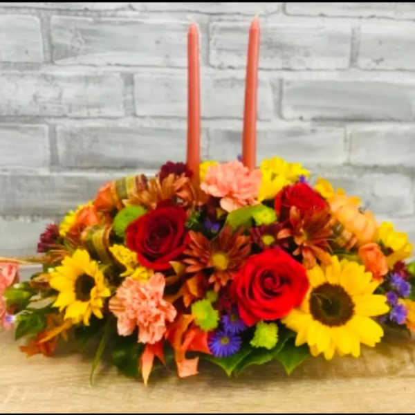 Low floral centerpiece with two orange taper candles and mixed blooms