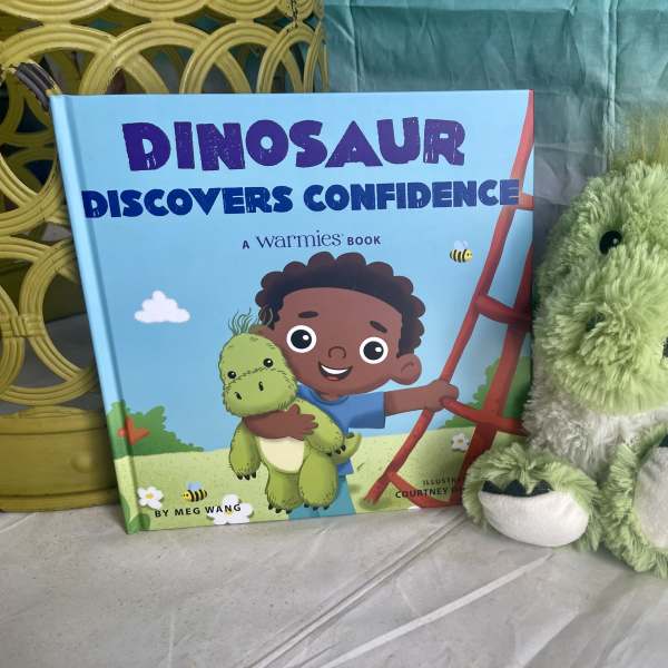 Children's dinosaur book beside a green plush dinosaur toy